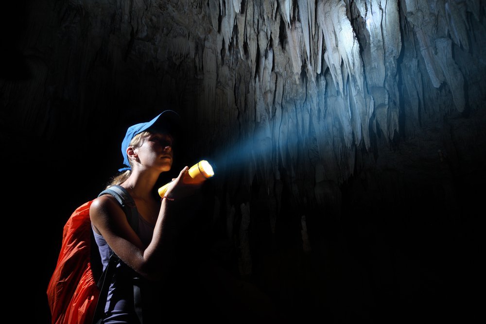 Žena s baterkou v jeskyni